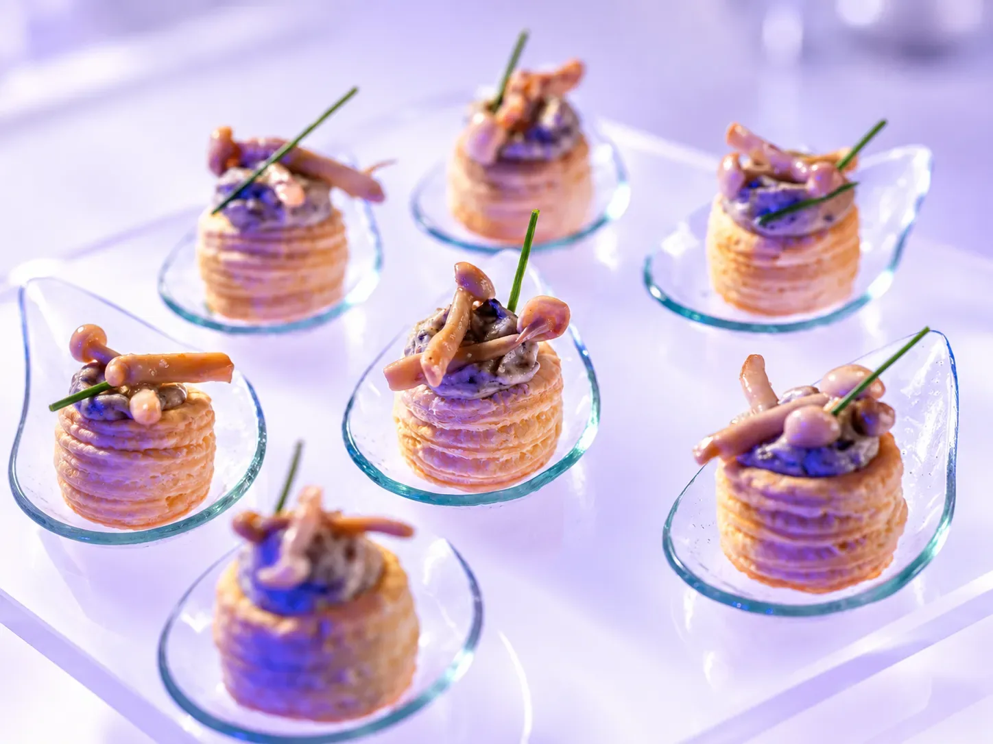 Mushroom vol-au-vent canapés topped with shimeji mushrooms and chives, each served on a glass spoon