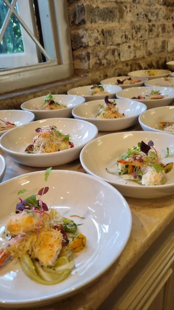 Individual bowls of gourmet shrimp appetizers garnished with microgreens on a serving counter.