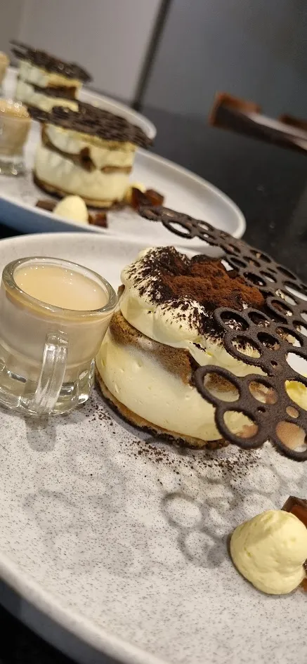 Tiramisu dessert topped with cocoa powder and chocolate decoration, served with a small espresso cup.
